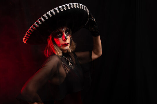 Mujer maquillada para d&iacute;a de muertos con sombrero charro sobre fondo negro y humo 