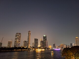 Nighttime scene of tall buildings adorned with lights by the riverside. Perfect for use as an illustration element or as a background