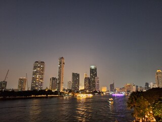Nighttime scene of tall buildings adorned with lights by the riverside. Perfect for use as an illustration element or as a background