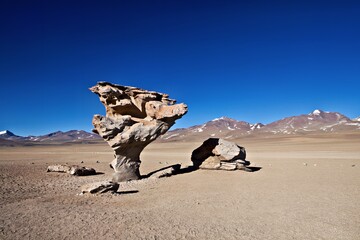 A unique rock formation in a vast desert landscape under a clear blue sky.