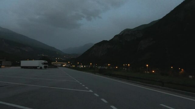 A tranquil parking lot for a TIR range in the Alps during dusk. Surrounded by towering mountains, the scene offers a peaceful and isolated atmosphere. Ideal for nature or outdoor activity footage