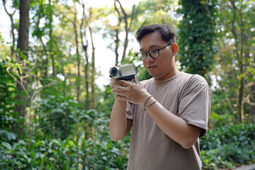 Young Asian man behind the camera directs and shoots the scene, video production enthusiast uses digital camcorder to capture footage.