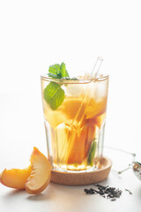 Fruit black iced tea with peaches and mint in a glass on the table. Summer drink concept