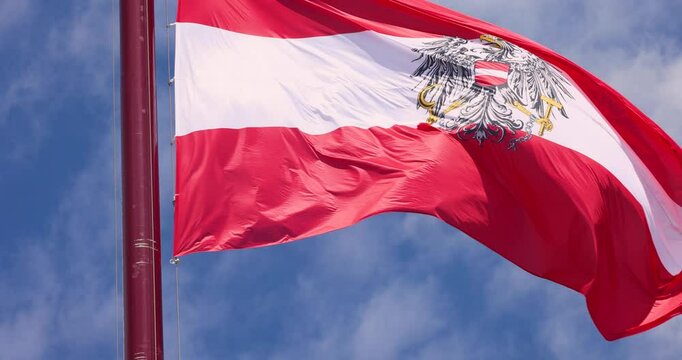 Austria Flag with Emblem waving on a pole with blue cloudy sky in the background Austria National Day