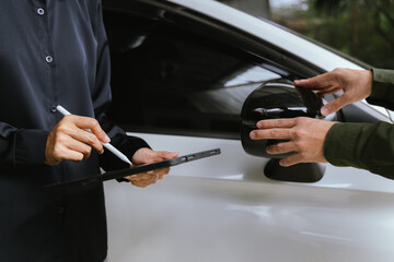 Insurance agent reviews car accident claim. Agent holds clipboard as customer signs form. Both discuss financial arrangements for damaged vehicle to ensure successful service.