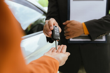 A businessman and his customer agree to a lease on a luxury car. The salesperson hands over the car keys as the customer signs a digital contract on a tablet to successfully close the sale.