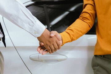 A businessman and his customer agree to a lease on a luxury car. The salesperson hands over the car keys as the customer signs a digital contract on a tablet to successfully close the sale.