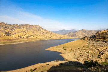A scenic view of Lake Kaweah and the surrounding golden hills near Three Rivers, California, showcasing the dry lakebed and the winding Kaweah River under the Sierra Nevada foothills.