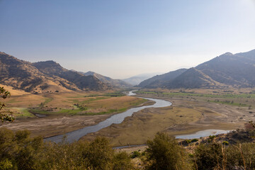 A scenic view of Lake Kaweah and the surrounding golden hills near Three Rivers, California, showcasing the dry lakebed and the winding Kaweah River under the Sierra Nevada foothills.