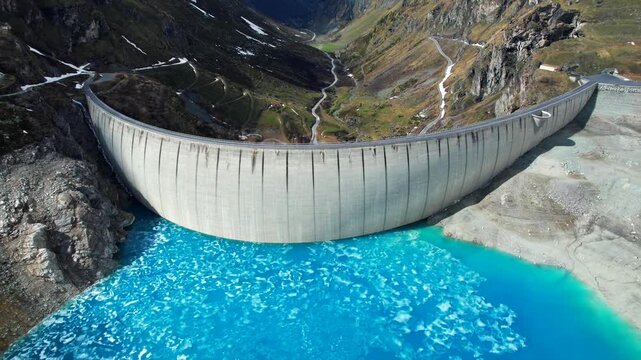 4k Drone Aerial Shot Of Vibrant Light Blue Glacial Water Of Lac de Moiry Dam With Vast Mountains And Zig-Zag Trail With Snow Covered peaks In Distance In Grimentz Switzerland