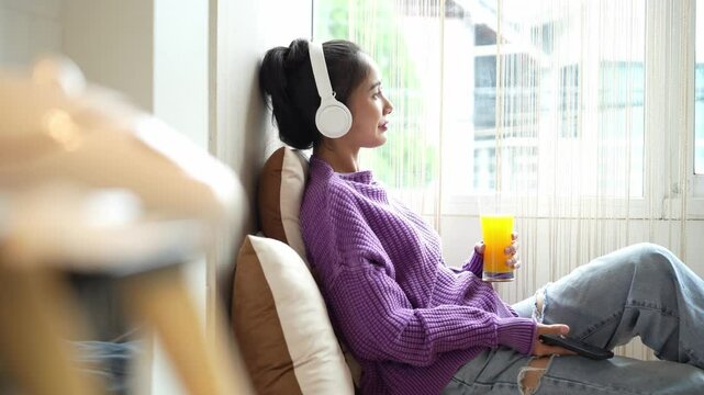 Asian woman leaning drink orange juice and listen to music