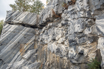 A detailed exploration of a marble quarry reveals vibrant patterns in stone, surrounded by greenery and a dynamic sky above