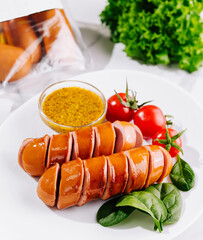 Sliced sausages on white plate with mustard greens and tomatoes