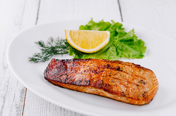 Grilled salmon steak lying on white plate with lemon and lettuce