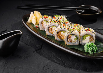 Sushi rolls covered with sesame seeds lying on a black plate on dark stone table