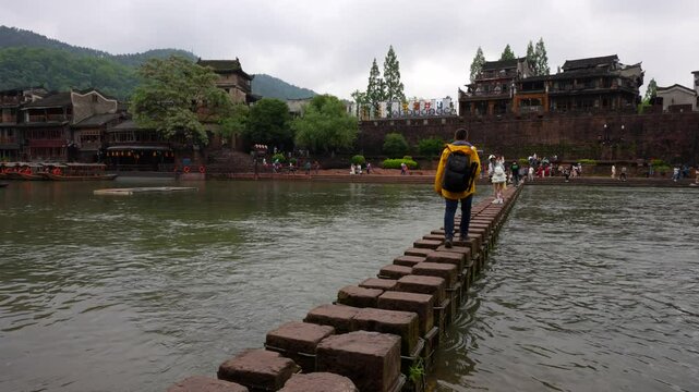 Traveler walking across Stepping Stones in Phoenix Ancient Town, China