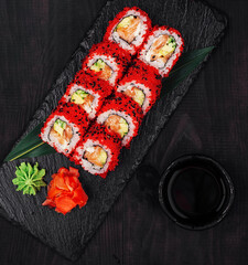 California uramaki sushi rolls with salmon and avocado decorated with red tobiko caviar on black slate plate