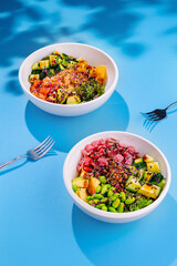 Two colorful bowls of poke on a vibrant blue background with forks resting nearby