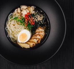 Steaming bowl of chicken ramen on black table setting