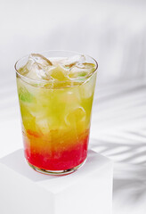 Colorful layered cocktail standing on white cube with tropical shadow