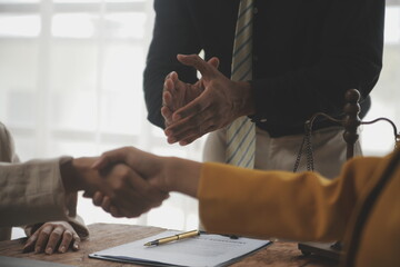 Obraz premium Lawyer shaking hands with a client making about documents, contracts, agreements, cooperation agreements with a female client at the lawyer's desk and a hammer at the table.