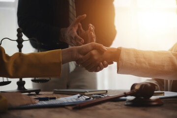 Lawyer shaking hands with a client making about documents, contracts, agreements, cooperation agreements with a female client at the lawyer's desk and a hammer at the table.