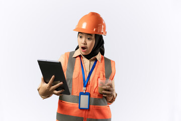 Young Indonesian female construction worker in hijab enjoying a cup of coffee while carrying a tablet, industrial and construction concept, isolated white background.
