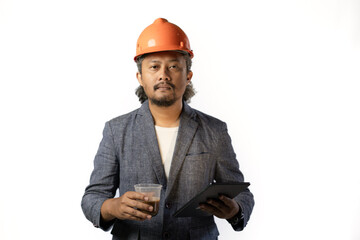 Indonesian male construction worker standing confidently and optimistically carrying a tablet and a cup of coffee, industrial and construction concept, isolated white background.
