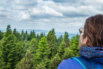 A woman enjoying a panoramic view of a lush forest landscape on a cloudy day from a scenic...