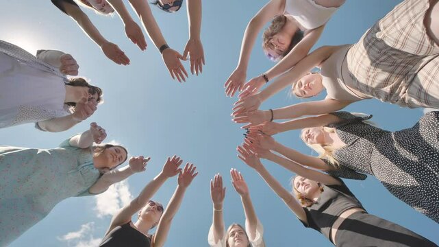 Group of friends is standing in a circle joining their hands together outdoors.
