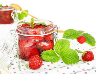 Delicious strawberry jam in traditional glass jar on white wooden background