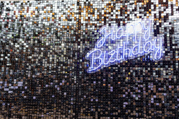 Happy Birthday lettering in LED strip light on sequin wall. Festive party decor.