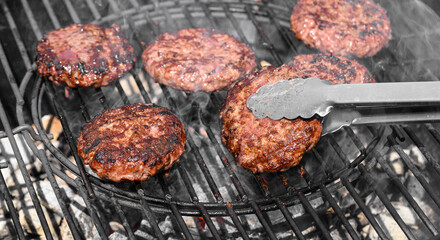 Kucharz przekręca grillowane na rozgrzanym ruszcie burgery wołowe, barbecue na świeżym powietrzu, majówka 