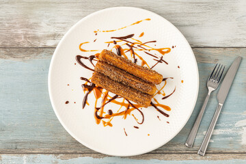 Hot churros with chocolate sauce on wooden table.