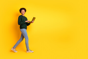 Naklejka premium Full size photo of nice young man use laptop walk empty space wear pullover isolated on yellow color background