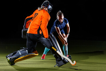 Goalkeeper and attacker engage in intense field hockey match against black background