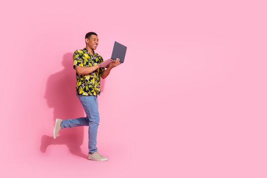 Full length photo of handsome young guy running netbook dressed stylish tropical print garment isolated on pink color background