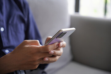 Man using smartphone chatting, checking social media by touch screen, He sitting on sofa in living room at home