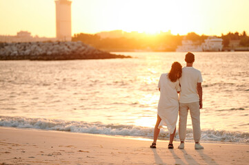 Silhouette couple standing on beach during sunset. Newlyweds in white robes admiring the sunset.