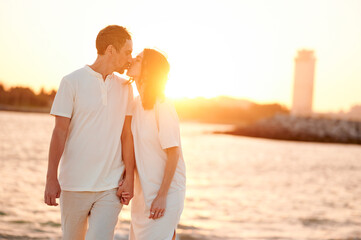 Сouple walking on beach at sunset. Family holidays on the coast. A kiss at sunset by the sea.