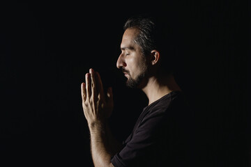 Man folded his hands in prayer on a black background. Low key male portrait.
