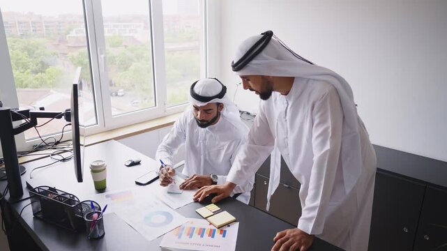 Cinematic video of two businessmen working together in a modern office in the united arab emirates. Business people with the traditional white kandura in Dubai.