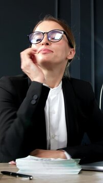Vertical video. A successful middle-aged businesswoman enjoys a wad of money from a successful deal and a concluded contract in her office. Ideal for themes of financial achievement and professionalis