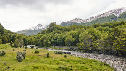  Cascada R&iacute;o Pipo flows through a lush green valley with snow-capped mountains in the background, creating a serene and picturesque natural scene