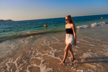 Young pretty woman in shorts and a top is walking on the sandy beach. Woman in Bikini Walking on Beach