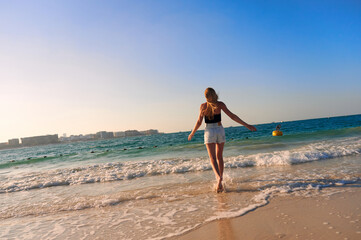 Happy young woman with hands up on sandy beach watching islands in the sea on sunny day. Hipster female on ocean shore having fun watching waves, sunbathing. Background, close up