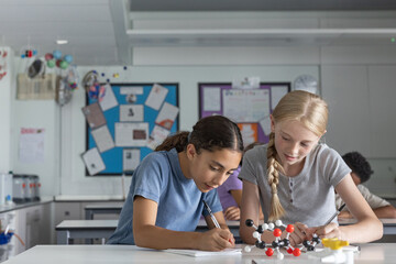 Two girl students in science class working on a project with a molecular model together