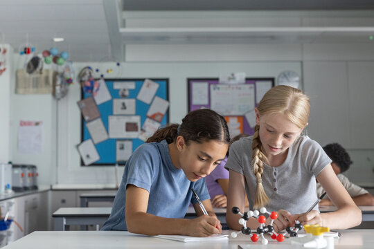 Two girl students in science class working on a project with a molecular model together - Powered by Adobe
