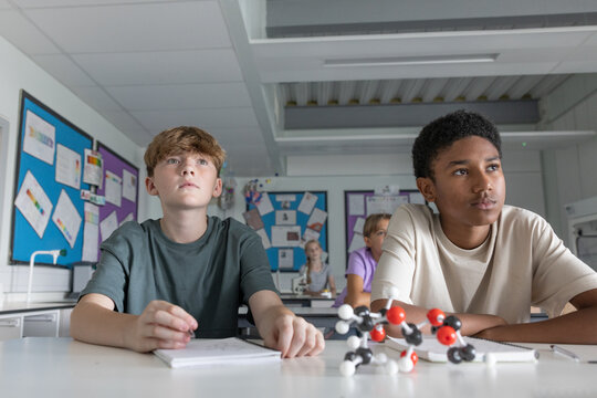 Two boy students listening in science class with a molecular model
