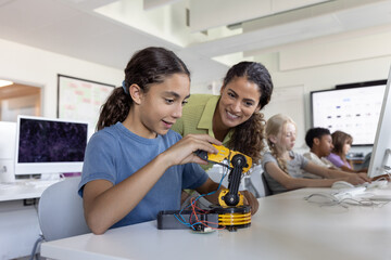 School girl showing teacher the robotic arm she is working on